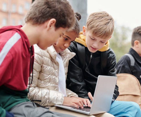 Drie kinderen geconcentreerd aan het samenwerken op een laptop, gezamenlijk bezig met educatieve activiteiten.
